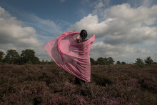 Rear View Of Woman In Dress Standing In Field Of Heather In Dress With Stola Under Cloudy Sky 