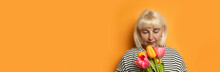 Happy Blonde 50s Mom Woman With Beautiful Bouquet Of Colored Tulips On Orange Background. Valentine's Day, Easter, Birthday, Happy Women's Day, Mother's Day.