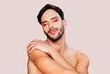 Portrait of gay man with beard, pink and yellow eyeshadow, eyes closed, no clothes. Beauty, make-up and skin care concept. Studio portrait, copy space.