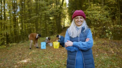 Wall Mural - Senior woman volunteer looking at camera when cleaning up forest from waste, community service concept.