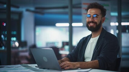 Modern Office Businessman or Manager Working on Computer, Smiling, Looking at Camera. Portrait of Successful IT Software Engineer in Glasses Working on a Laptop at his Desk.