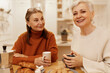 © shurkin_son - Portrait of two confident successful women in their 50s sitting at cozy cafe having breakfast together, drinking morning coffee with baking goods, talking, sharing news. People and lifestyle