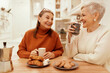 © shurkin_son - People, lifestyle and leisure concept. Portrait of stylish senior women in cozy sweaters having breakfast together at cafe, sitting at wooden table, sharing news, drinking coffee with pastries