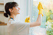 © Drobot Dean - White young woman in gloves smiling while cleaning window