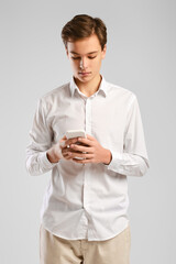 Wall Mural - Handsome young man in white shirt and trousers texting on smartphone