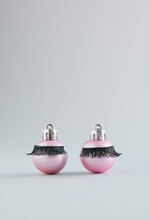 Pink Christmas Baubles With False Eyelashes On A Grey Background. New Year Aesthetic Concept With Copy Space.