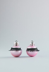 Wall Mural - Pink Christmas baubles with false eyelashes on a grey background. New Year aesthetic concept with copy space.