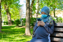 Muslim pregnant woman wearing face mask texting or browsing on the smartphone