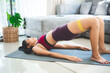 © chokniti - Young fit and healthy Asian woman in sportswear practicing bridge pose yoga on mat with resistance rubber band on thighs for wellbeing