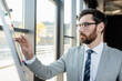 © LIGHTFIELD STUDIOS - Businessman in formal wear standing near flip chart in office.