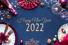 Happy New Year 2021 Gilded Text In Frame Made From Silvester Party Table Setup. Vine, Glasses, Plates, Fork, Knife. Xmas Decorations And Garland. Flat Lay In Golden And Red On Classic Blue Textile.