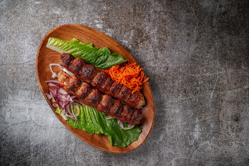 Wall Mural - Meat kebab and barbecue with onions, Korean carrots and green salad in a plate against the background of a gray stone table 