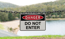 Danger Do Not Enter Sign Attached To A Chain With A Dam In The Background