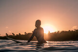 Fototapeta Sawanna - Portrait of blond surfer girl on white surf board in blue ocean pictured from the water at golden sunrise time in Encuentro beach