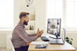 Business adviser or manager sitting at desk with calculator, looking at computer, having conversation with team of businesspeople in remote videocall work meeting or videoconference webinar, side view
