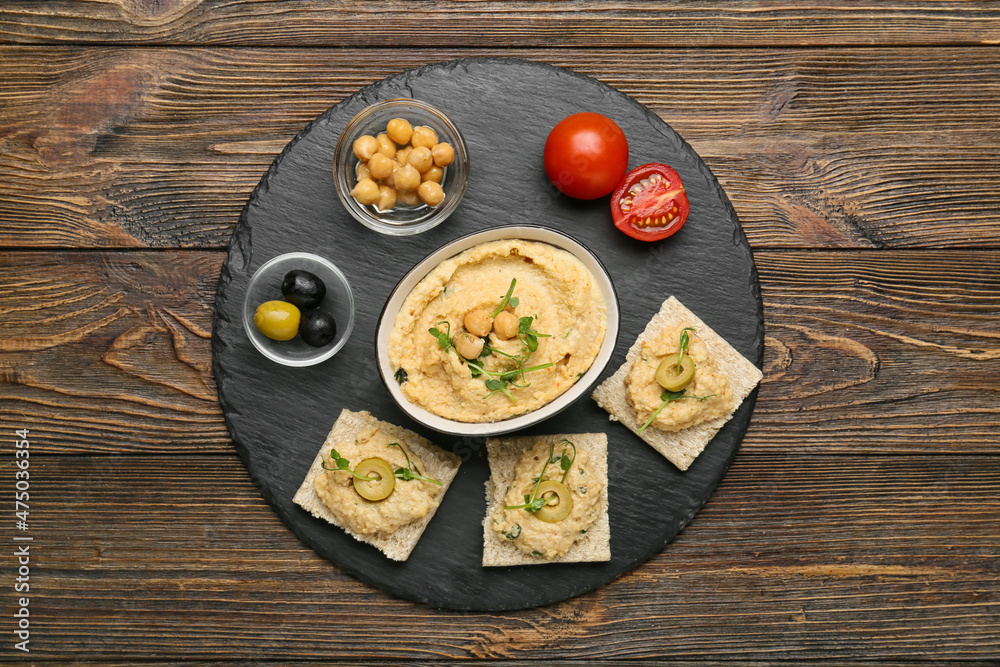 Bowl with delicious hummus, crackers and olives on wooden background