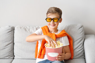 Sticker - Little boy in eyeglasses with tasty popcorn sitting on sofa near light wall