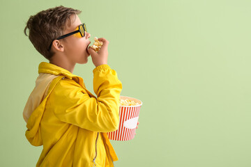 Sticker - Little boy in eyeglasses eating tasty popcorn on green background