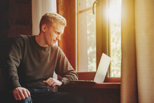 Portrait Of Young Businessman With Laptop At Window Of Living Room
