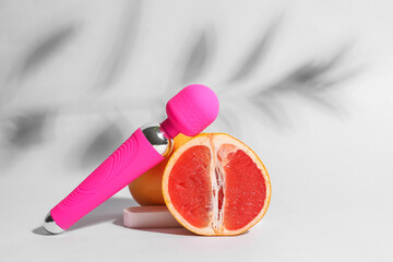 Clitoral vibrator from sex shop and juicy grapefruits on light background