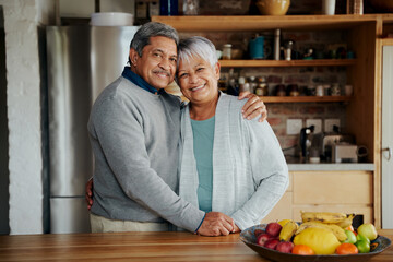 Portrait of happily retired elderly biracial couple holding each other. Healthy lifestyle, standing in modern kitchen.