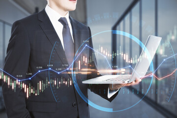 Poster - Businessman holding laptop computer with glowing forex chart trading interface on blurry office interior background. Market, economy and data exchange concept. Double exposure.