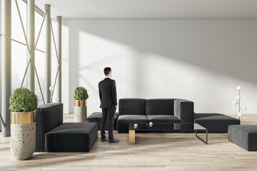 Aufkleber - Thoughtful young businessman standing in modern living room or business hall interior with sunlight, window with panoramic city view, furniture and mock up place on concrete wall, wooden flooring.