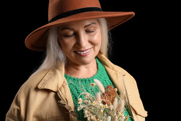 Poster - Fashionable mature woman in felt hat holding bouquet of flowers on dark background