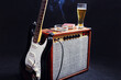 Amplifier for guitar with black guitar, glass of beer and smoking cigarette on black background.