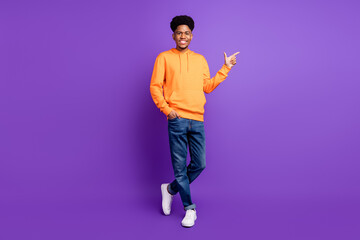 Wall Mural - Full size photo of young dark skin happy man point finger empty space advertise wear jeans isolated on violet color background