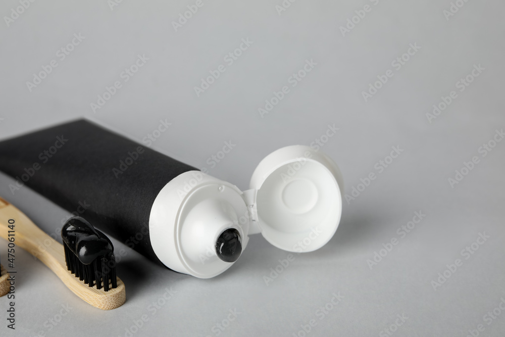Tube with black tooth paste and bamboo brush on grey background