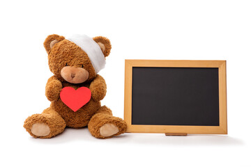 Wall Mural - medicine, healthcare and childhood concept - chalkboard and teddy bear toy with bandaged head holding red heart on white background