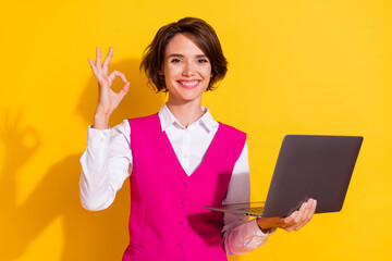 Photo of excited shiny young lady wear pink suit holding modern device showing okey smiling isolated yellow color background
