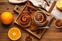 Glass Cup Of Tasty Orange Tea With Cinnamon And Roll On Wooden Background