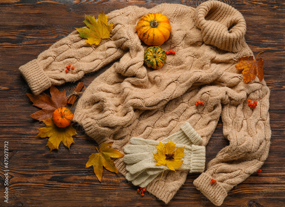 Warm sweater, gloves and autumn decor on wooden background