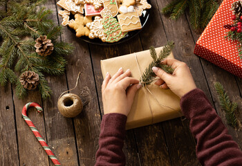 Wall Mural - Woman decorating a Christmas present with conifer evergreen branch on a wooden table background