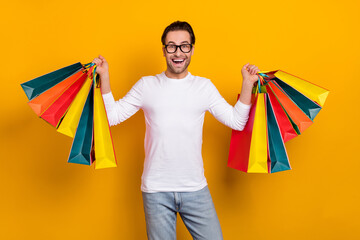 Sticker - Photo of nice brunet millennial guy hold bags wear eyewear white outfit isolated on vibrant yellow color background