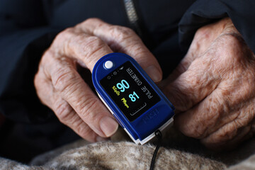 Digital finger oximeter on hand of an elderly woman. Monitoring of pulse and blood oxygen levels at home