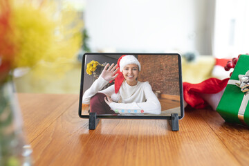 Wall Mural - Happy caucasian woman in santa hat waving on tablet video call screen at christmas time