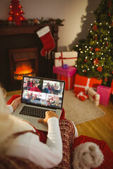 Wall Mural - Santa claus making laptop christmas group video call with four waving families