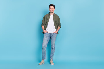 Canvas Print - Photo of pretty attractive young guy wear green shirt arms pockets walking smiling isolated blue color background