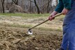 A farmer in a field hoeing the soil by hand before planting the seeds in the spring