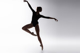 silhouette of young ballerina in bodysuit dancing on gray