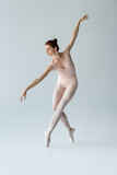 full length of flexible and young ballerina in bodysuit dancing on grey