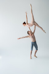 Wall Mural - full length of shirtless ballet dancer lifting graceful ballerina in bodysuit on gray