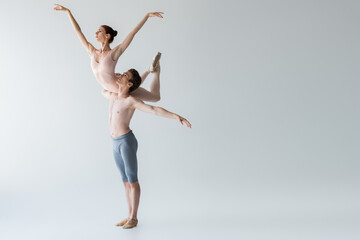 Wall Mural - full length of shirtless ballet dancer lifting ballerina isolated on grey