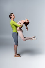 Wall Mural - strong ballet dancer lifting ballerina in bodysuit on grey