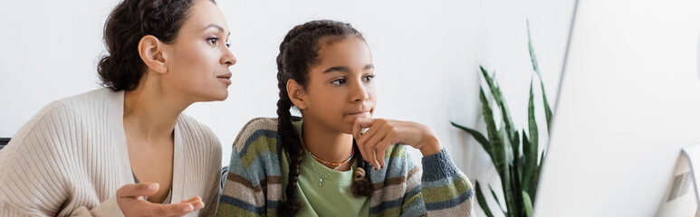 african american woman pointing at computer monitor near thoughtful daughter, banner