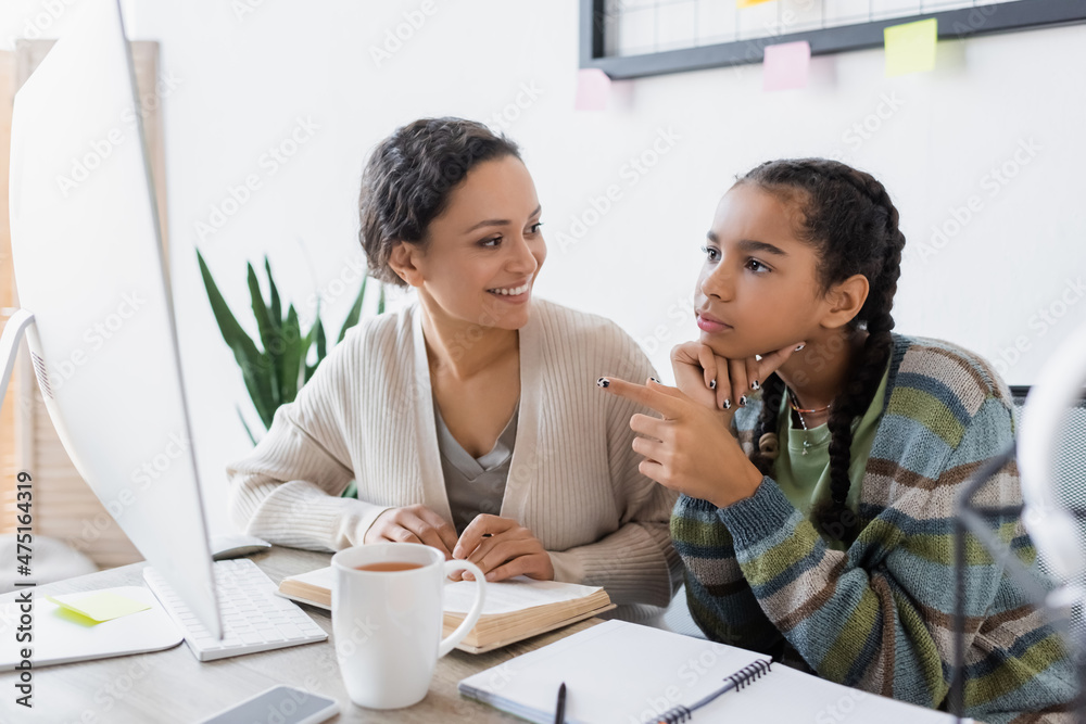 african american girl pointing at computer monitor while doing homework ...
