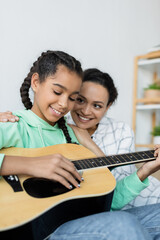 Wall Mural - african american teenage girl playing acoustic guitar near happy mom at home